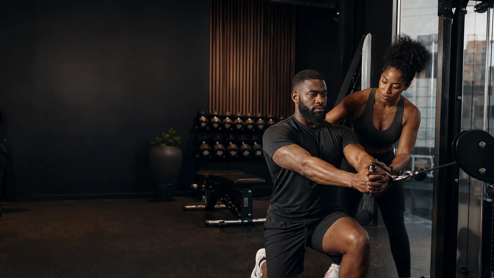 A coach guides an adult client through a cable strength exercise in a private training studio
